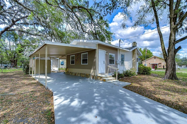 view of front facade featuring an attached carport, concrete driveway, an outdoor structure, and a chimney