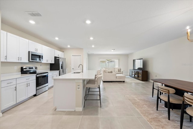 kitchen featuring visible vents, a kitchen bar, an island with sink, appliances with stainless steel finishes, and a sink