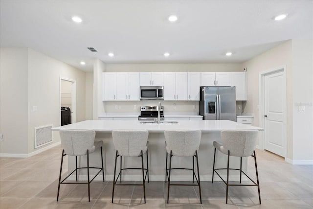 kitchen featuring visible vents, a center island with sink, a sink, white cabinetry, and appliances with stainless steel finishes