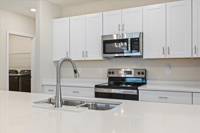 kitchen with a sink, washing machine and dryer, appliances with stainless steel finishes, white cabinets, and light countertops