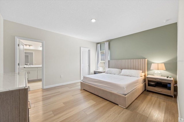 bedroom featuring ensuite bathroom, light wood-type flooring, and baseboards