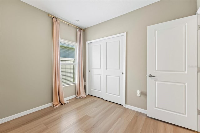 unfurnished bedroom featuring light wood-style floors, baseboards, and a closet