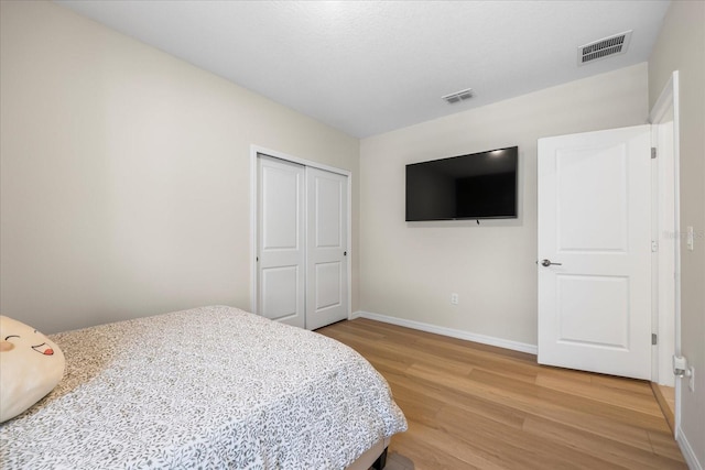 bedroom featuring light wood-type flooring, visible vents, baseboards, and a closet