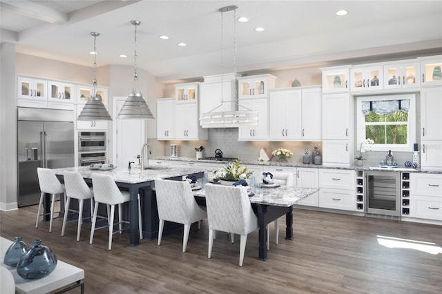 kitchen with beverage cooler, an island with sink, a sink, appliances with stainless steel finishes, and wall chimney range hood