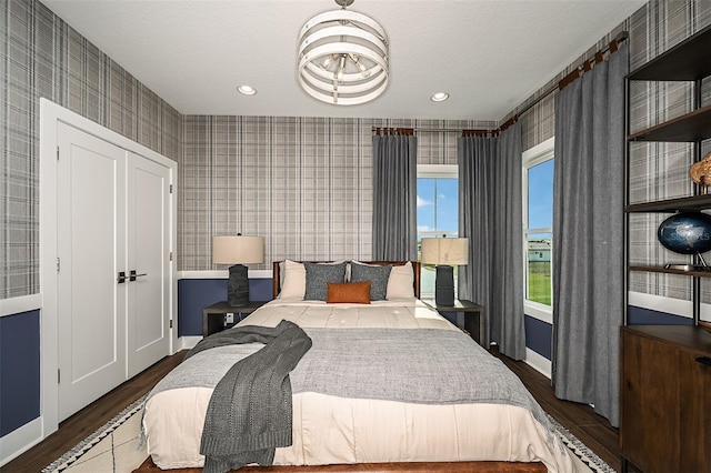 bedroom featuring a textured ceiling, wallpapered walls, baseboards, and wood finished floors