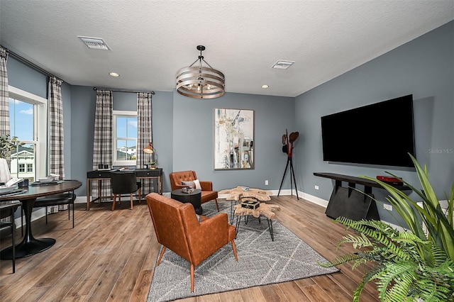 living room featuring a textured ceiling, wood finished floors, visible vents, and baseboards