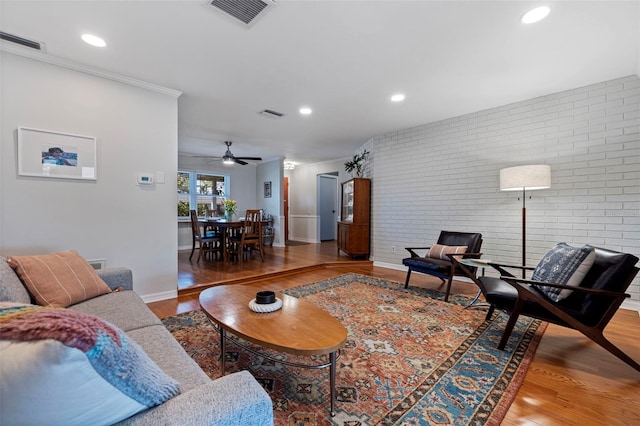 living area featuring wood finished floors, visible vents, brick wall, and baseboards