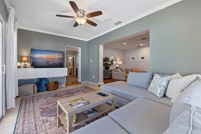 living area with tile patterned flooring, visible vents, crown molding, and ceiling fan