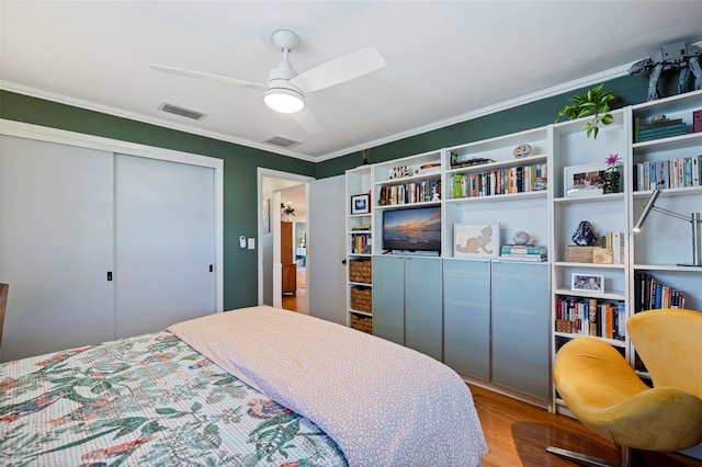 bedroom featuring a closet, visible vents, ornamental molding, and wood finished floors