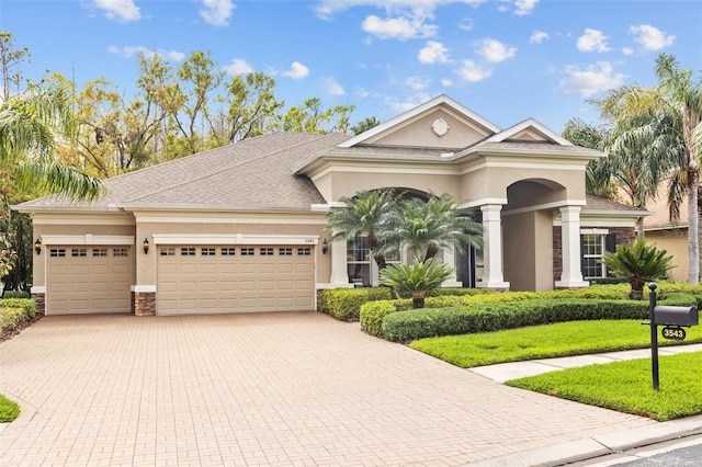 mediterranean / spanish home with stone siding, stucco siding, an attached garage, and decorative driveway