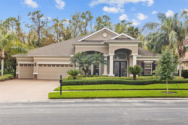 view of front of home featuring decorative driveway, a front lawn, an attached garage, and stucco siding