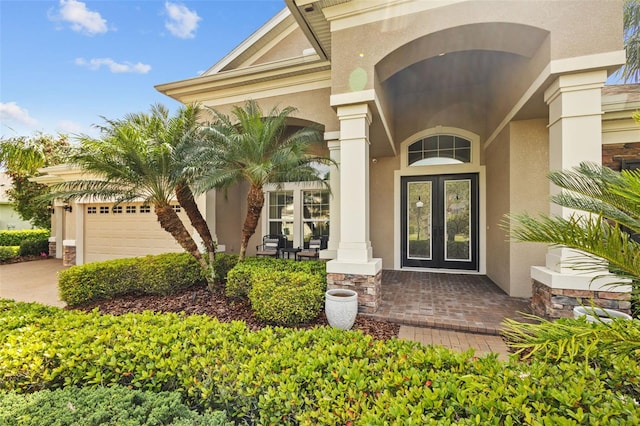 entrance to property featuring driveway, an attached garage, stucco siding, french doors, and stone siding