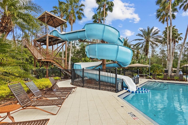 community pool with a patio area, stairway, fence, and a water slide