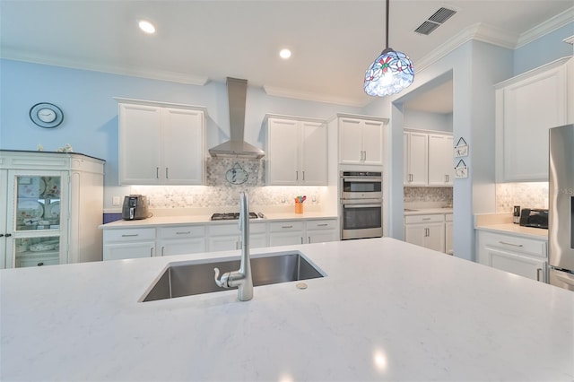 kitchen featuring visible vents, wall chimney range hood, ornamental molding, white cabinets, and a sink