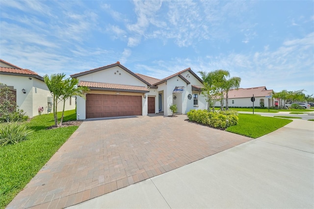 mediterranean / spanish home featuring a tile roof, a front yard, stucco siding, decorative driveway, and an attached garage