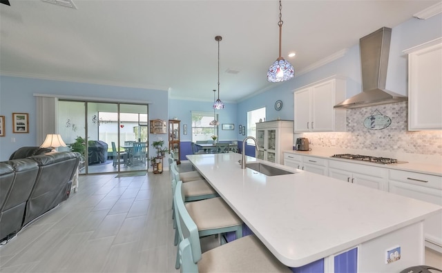 kitchen featuring a sink, wall chimney range hood, tasteful backsplash, open floor plan, and light countertops