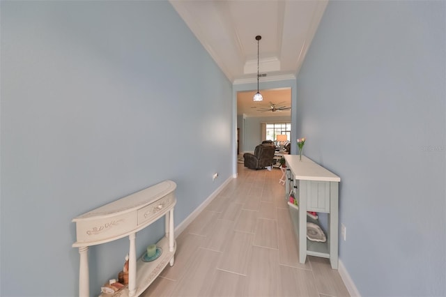 hall with a raised ceiling, baseboards, and ornamental molding