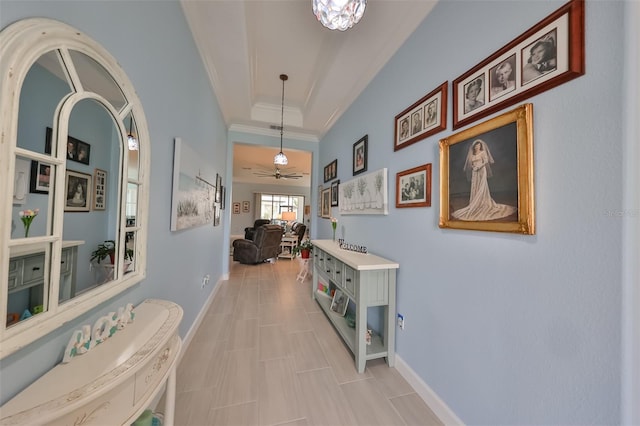 corridor with a raised ceiling, baseboards, and ornamental molding