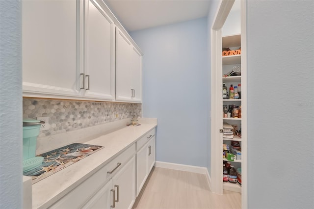 kitchen with decorative backsplash, white cabinetry, light countertops, and baseboards