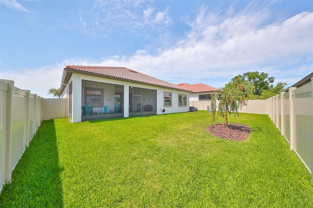 back of house featuring a tiled roof, stucco siding, a lawn, a fenced backyard, and a sunroom