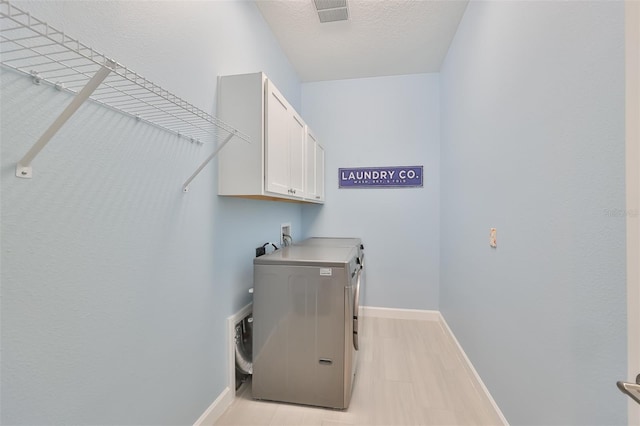 clothes washing area with visible vents, cabinet space, baseboards, and separate washer and dryer