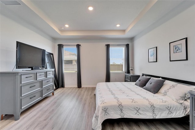 bedroom with a tray ceiling, recessed lighting, light wood-type flooring, baseboards, and visible vents