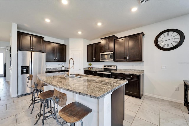 kitchen featuring light stone counters, a sink, a breakfast bar area, stainless steel appliances, and dark brown cabinets