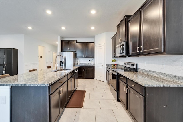 kitchen with a sink, light stone counters, dark brown cabinets, and appliances with stainless steel finishes
