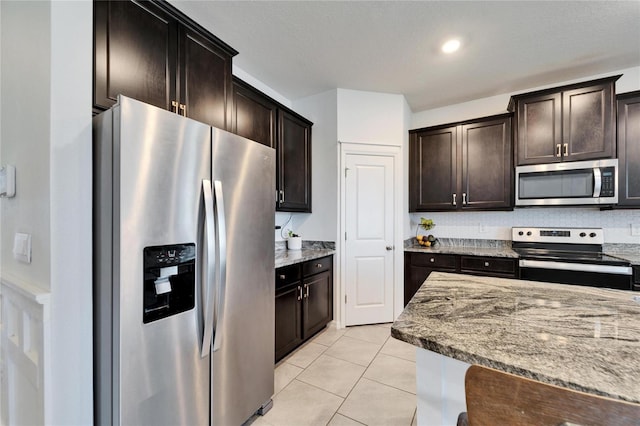 kitchen with dark brown cabinetry, light stone countertops, light tile patterned floors, and appliances with stainless steel finishes