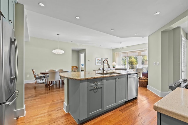 kitchen with light wood-style flooring, gray cabinets, a sink, appliances with stainless steel finishes, and light stone countertops