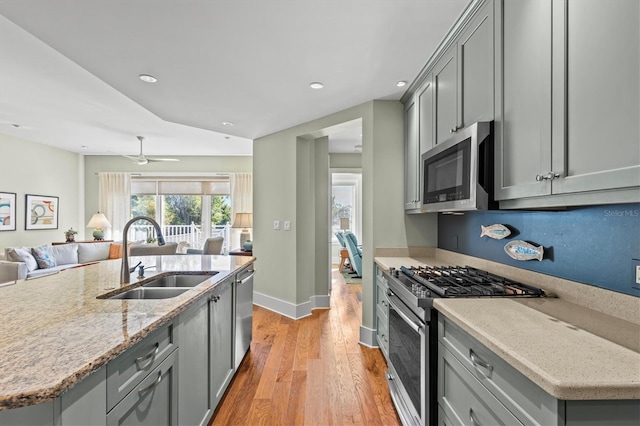 kitchen featuring a sink, gray cabinetry, stainless steel appliances, light wood-style floors, and open floor plan