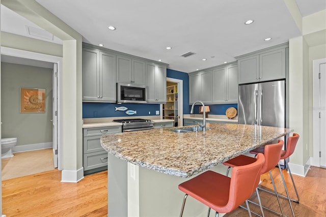 kitchen featuring light stone counters, light wood finished floors, gray cabinetry, a sink, and appliances with stainless steel finishes