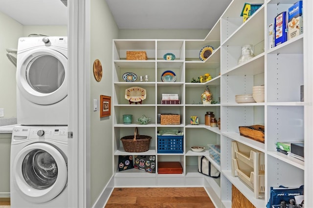 laundry room featuring baseboards, stacked washer and clothes dryer, wood finished floors, and laundry area