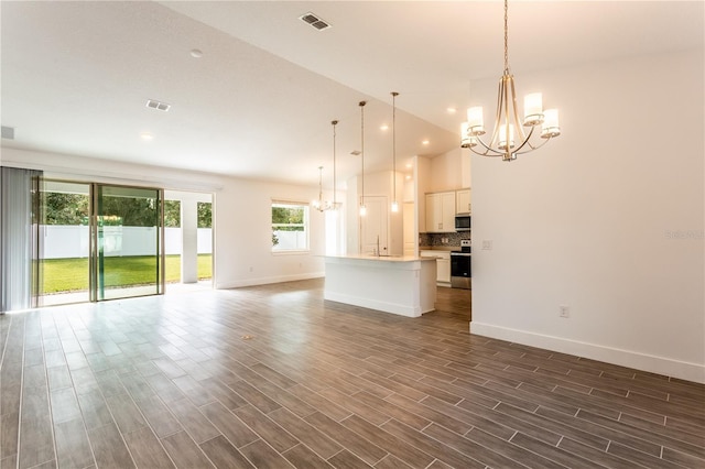 unfurnished living room featuring wood finish floors, visible vents, and an inviting chandelier