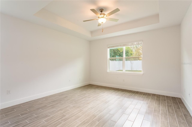 spare room featuring a tray ceiling, baseboards, light wood-type flooring, and ceiling fan