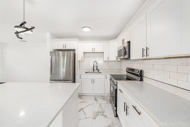 kitchen with marble finish floor, a sink, white cabinetry, appliances with stainless steel finishes, and decorative backsplash