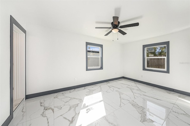 empty room featuring a wealth of natural light, marble finish floor, a ceiling fan, and baseboards