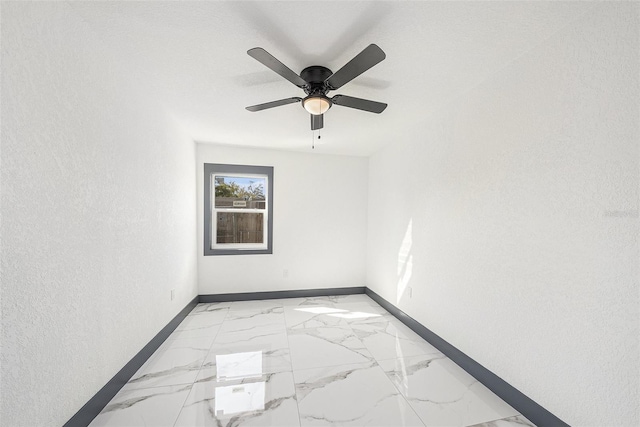 unfurnished room featuring a textured wall, marble finish floor, baseboards, and ceiling fan