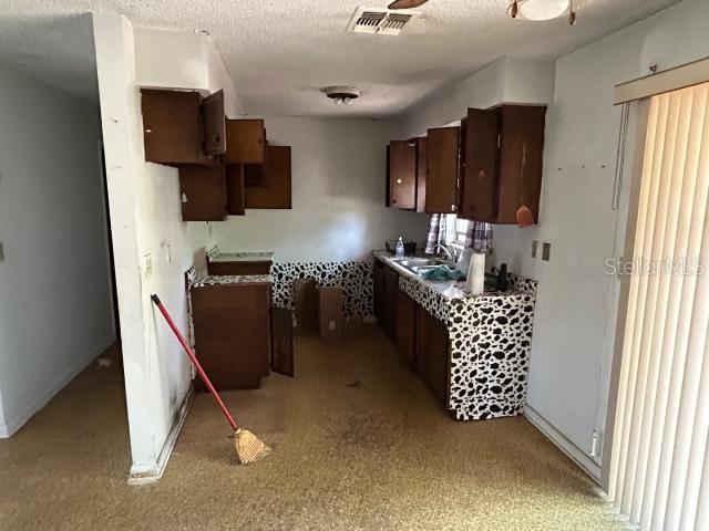 kitchen with visible vents, a sink, a textured ceiling, dark brown cabinetry, and baseboards