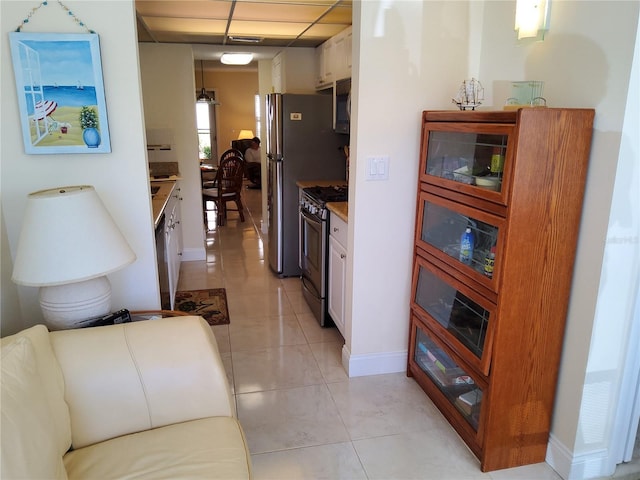 kitchen with baseboards, a drop ceiling, light tile patterned flooring, white cabinets, and stainless steel appliances