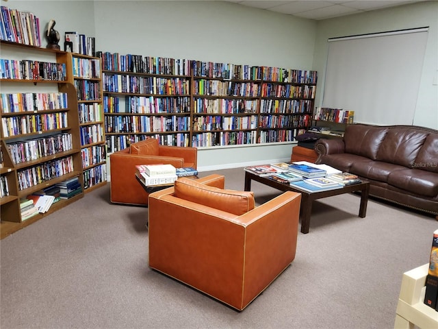 sitting room with a paneled ceiling, carpet, and wall of books