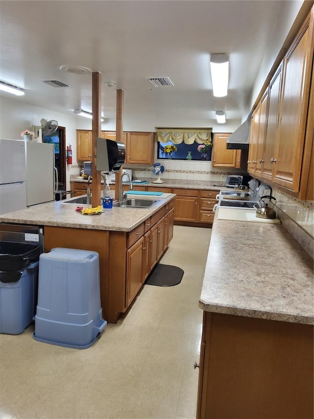 kitchen with visible vents, an island with sink, a sink, backsplash, and light countertops