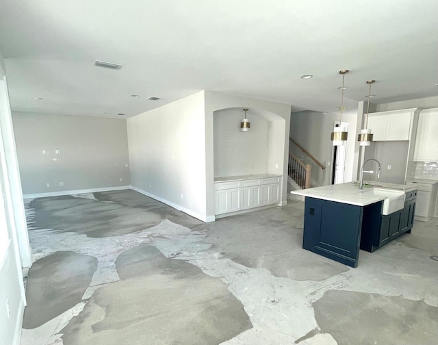 kitchen featuring visible vents, a kitchen island with sink, a sink, light countertops, and concrete flooring