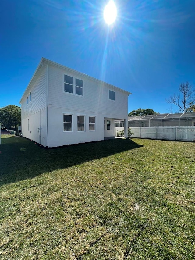 rear view of property featuring a lawn and fence