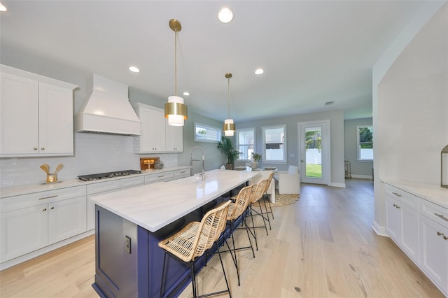 kitchen featuring tasteful backsplash, stainless steel gas cooktop, light wood-style flooring, premium range hood, and white cabinetry