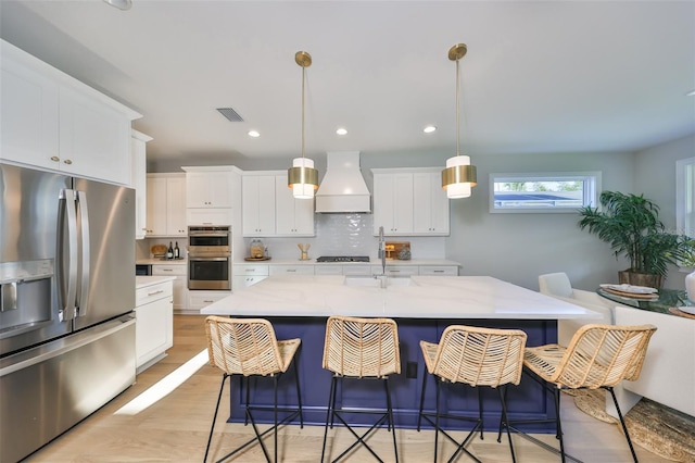 kitchen featuring a sink, visible vents, white cabinetry, appliances with stainless steel finishes, and premium range hood