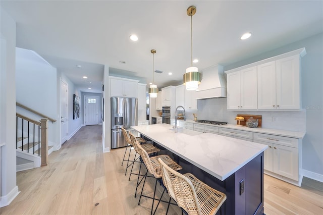 kitchen featuring premium range hood, light wood-style flooring, appliances with stainless steel finishes, and a sink