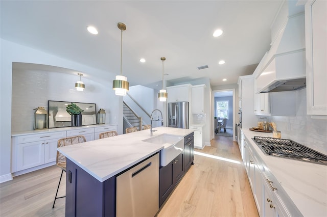 kitchen featuring light wood finished floors, a sink, decorative backsplash, appliances with stainless steel finishes, and custom exhaust hood
