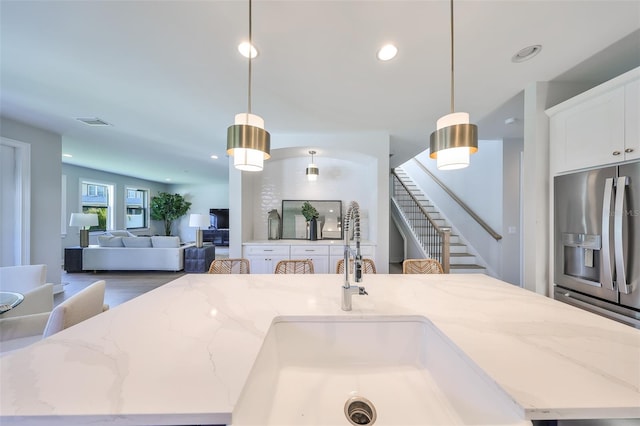 kitchen with decorative light fixtures, stainless steel refrigerator with ice dispenser, a center island with sink, and visible vents
