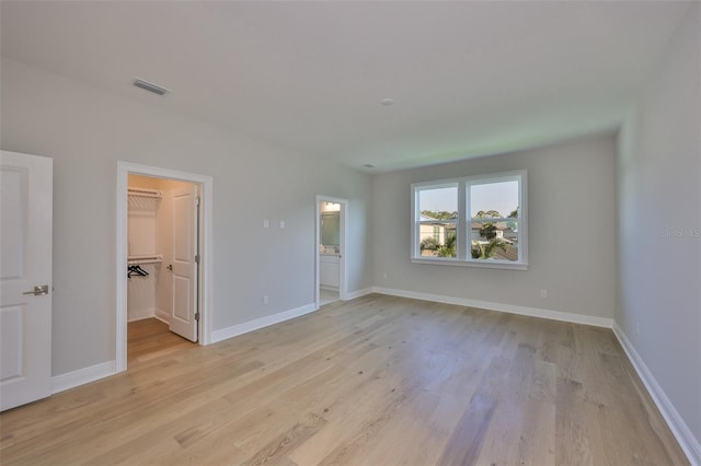 unfurnished bedroom featuring light wood-style flooring, a spacious closet, baseboards, and visible vents